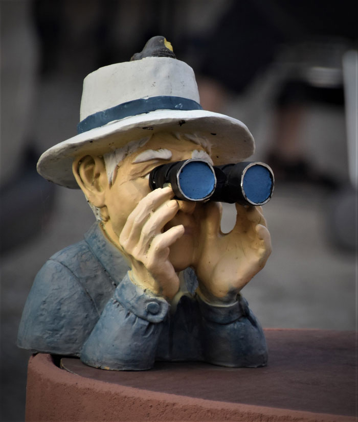 Figur eines älteren Menschen mit Hut, der durch ein Fernglas späht.